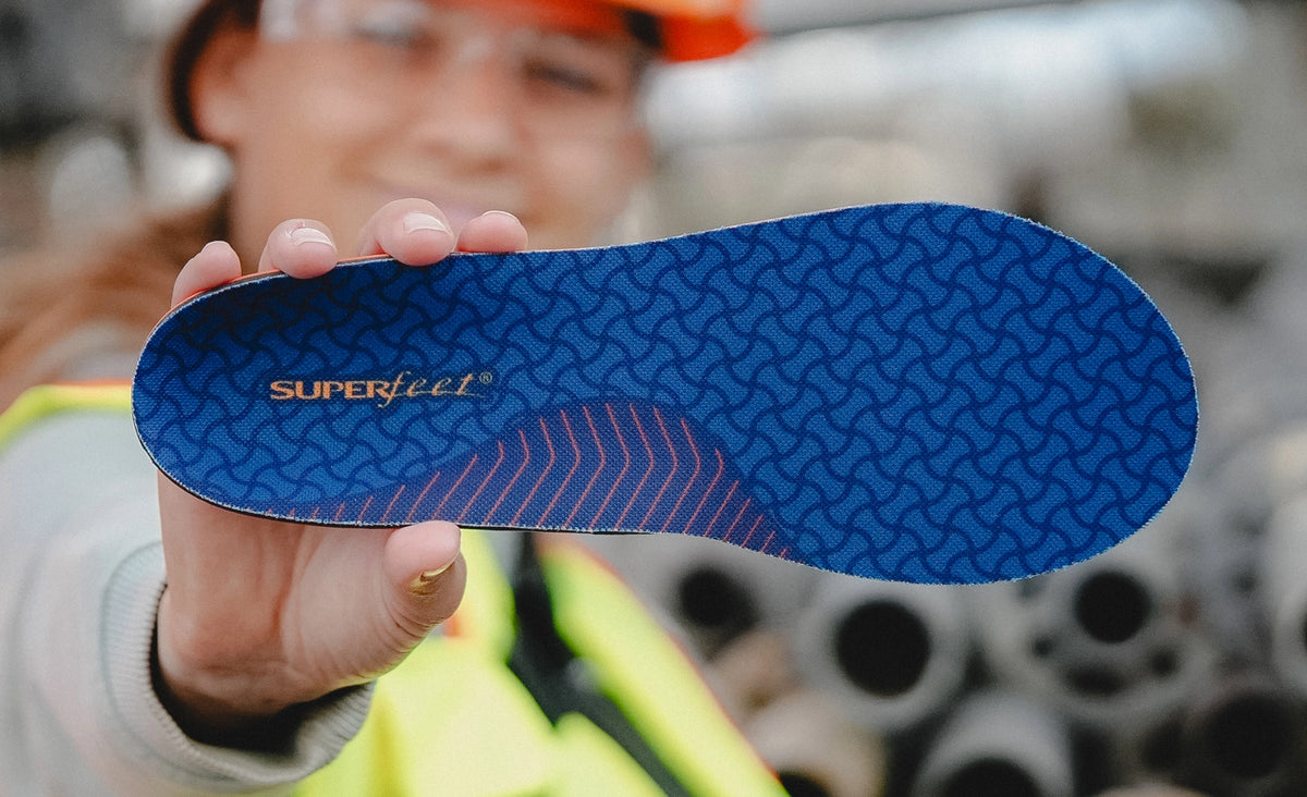 A worker standing outside holding up Superfeet Work Cushion insole to the camera.