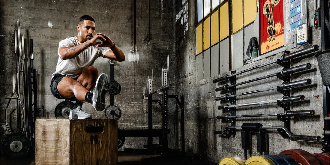 Man in gym on jump box practicing one legged squat sits for balance and stability while wearing Superfeet insoles and orthotics.