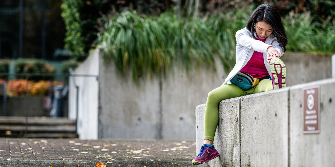 Woman sitting on concrete barrier doing leg stretches while wearing Superfeet insoles.