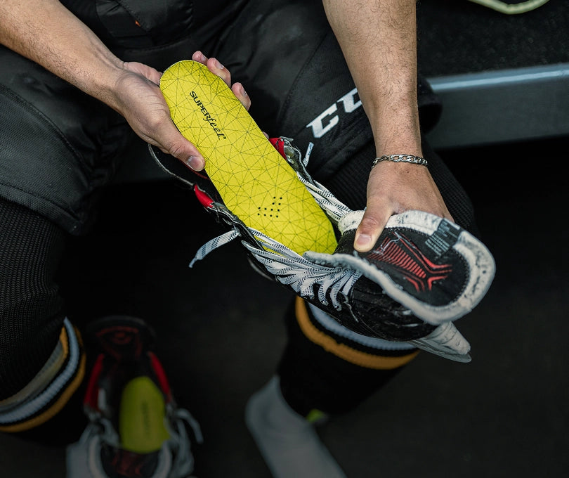 A ice hockey player sitting on a bench while inserting Superfeet's Hockey Cushion Insole. 