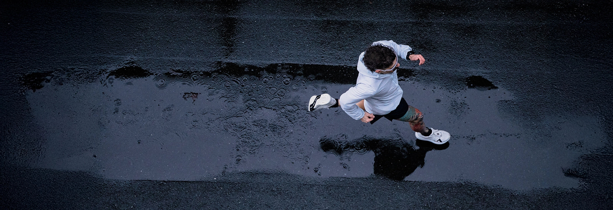 Birds eye view of a man running on wet pavement in the rain. 